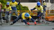 Four workers smooth our concrete for a slab.  One man is bending over and drawing a tool over the concrete to smooth it.  The other three workers are waiting to assist.